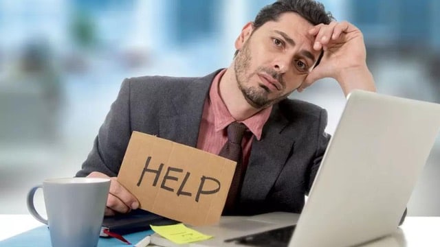 Despondent businessman holding a 'HELP' sign at his desk, highlighting the need to effectively communicate with investors after funding.