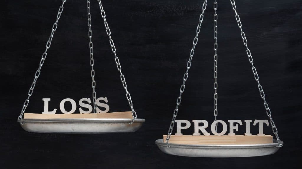 Image of a balanced scale with the words "Loss" and "Profit" on opposite sides, symbolizing the financial risks and rewards in real estate flipping land vs houses